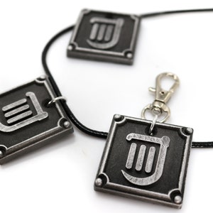 May include: A black leather necklace with three silver pendants featuring a stylized lyre symbol. The pendants are square shaped with rounded corners and have a silver finish.