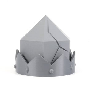 May include: A gray 3D printed crown with a pointed top and a jagged edge. The crown has a decorative design with a series of points around the base.