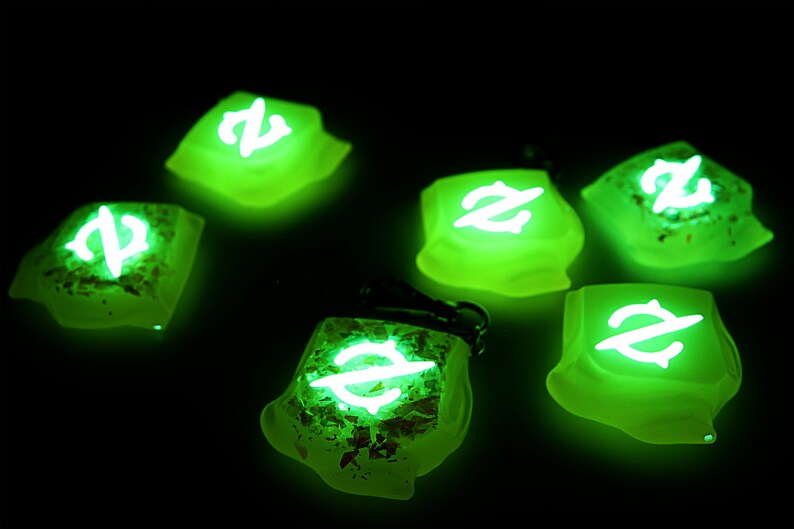 May include: Six green glow-in-the-dark dice with a white symbol on each face. The symbol is a stylized letter Z with a line through it.