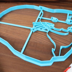 May include: A light blue plastic cookie cutter shaped like a cat's face. The cutter has a detailed design with a cat's eyes, nose, whiskers, and ears.
