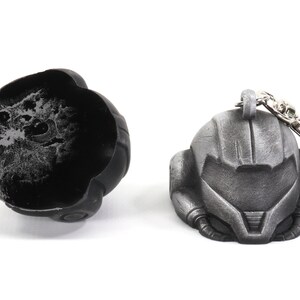 Puede incluir: Un llavero de metal plateado que presenta una r&eacute;plica detallada de un casco del videojuego Metroid. El llavero est&aacute; unido a un anillo de metal plateado.