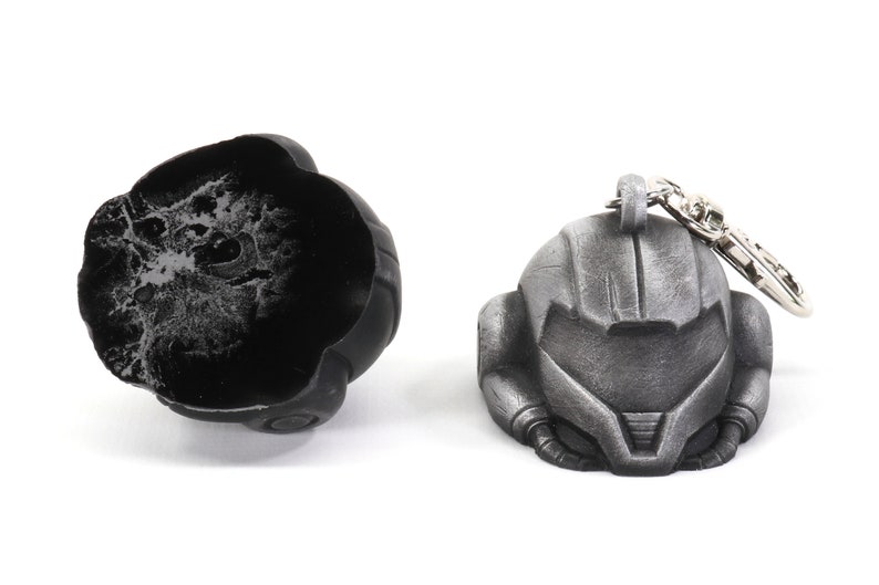 Puede incluir: Un llavero de metal plateado que presenta una r&eacute;plica detallada de un casco del videojuego Metroid. El llavero est&aacute; unido a un anillo de metal plateado.