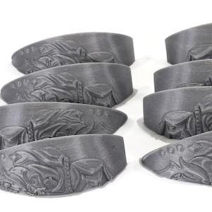 May include: Eight grey 3D printed decorative pieces with an intricate design. The pieces are shaped like a curved, flat surface.