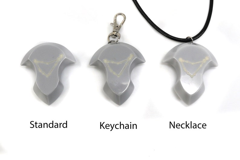 May include: Three versions of a silver-colored pendant with a white design. The pendant is available as a standard piece, a keychain, and a necklace.