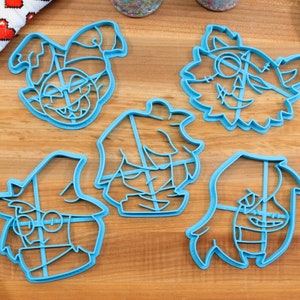 May include: Set of five blue plastic cookie cutters shaped like cartoon characters. The characters have different facial expressions and hairstyles.