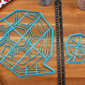 May include: Two blue plastic snowflake cookie cutters on a wooden surface. The larger cutter has a more intricate design than the smaller cutter.
