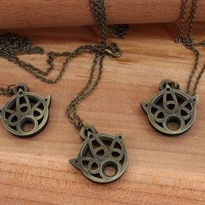 May include: Three bronze necklaces with intricate circular pendants featuring a geometric design. The pendants are hollow and have a circular opening in the center.