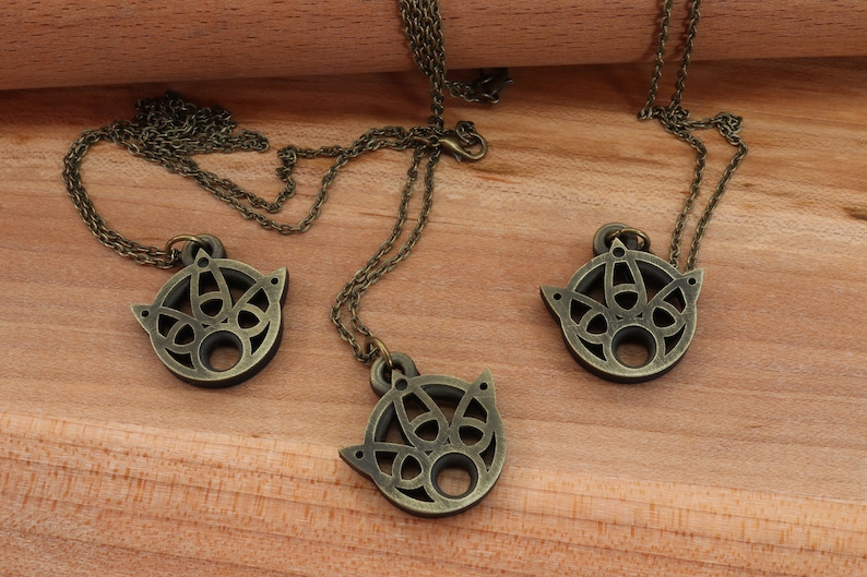 May include: Three bronze necklaces with intricate circular pendants featuring a geometric design. The pendants are hollow and have a circular opening in the center.