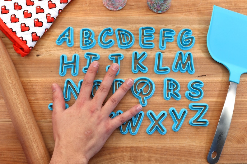 Op de afbeelding: Een set blauwe plastic alfabetkoekjesvormen op een houten oppervlak. De vormen zijn alfabetisch gerangschikt.