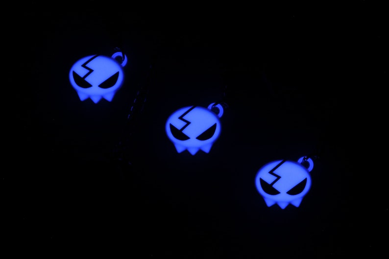 May include: Three glow-in-the-dark blue skull charms with a lightning bolt design. The charms are hanging from black cords.