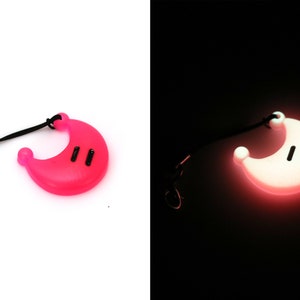 K&ouml;nnte beinhalten: Ein rosa halbmondf&ouml;rmiger Schl&uuml;sselanh&auml;nger mit einer schwarzen Schnur und einem silbernen Clip. Der Schl&uuml;sselanh&auml;nger leuchtet im Dunkeln.