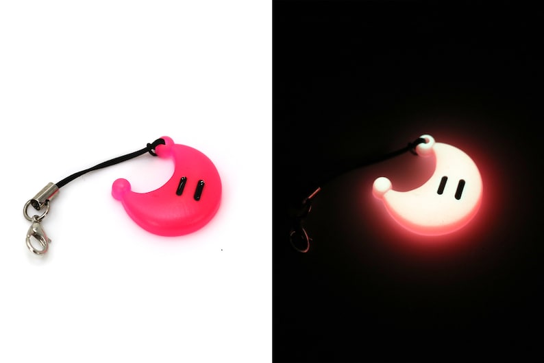K&ouml;nnte beinhalten: Ein rosa halbmondf&ouml;rmiger Schl&uuml;sselanh&auml;nger mit einer schwarzen Schnur und einem silbernen Clip. Der Schl&uuml;sselanh&auml;nger leuchtet im Dunkeln.