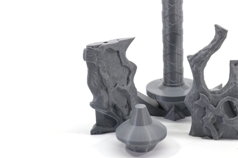 May include: A set of four gray 3D printed pieces that appear to be parts of a fantasy weapon or prop. The pieces are made of a smooth, plastic-like material and have intricate details.
