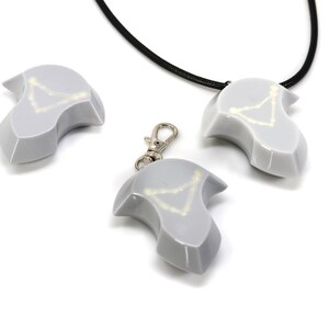 May include: Three gray ceramic pendants with a white constellation design. One pendant is on a black cord, one is on a silver chain, and one is on a silver keychain.