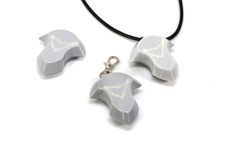 May include: Three gray ceramic pendants with a white constellation design. One pendant is on a black cord, one is on a silver chain, and one is on a silver keychain.