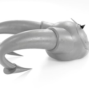 May include: A silver-colored, stylized, abstract sculpture with two horns. The sculpture is made of a smooth, metallic material and has a sharp, pointed tip on the top.