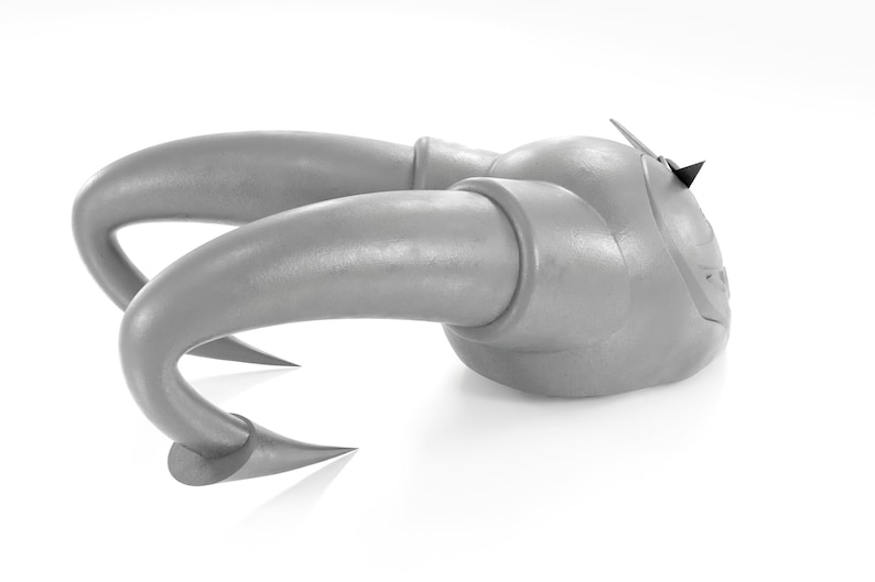 May include: A silver-colored, stylized, abstract sculpture with two horns. The sculpture is made of a smooth, metallic material and has a sharp, pointed tip on the top.