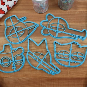 May include: A set of six blue plastic cookie cutters shaped like cartoon characters. The characters include a bear wearing a cowboy hat and glasses, a wolf, a cat, a crocodile, and a bird wearing a hat.