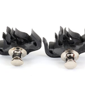 May include: Two black flame-shaped metal clasps with silver push-button closures.