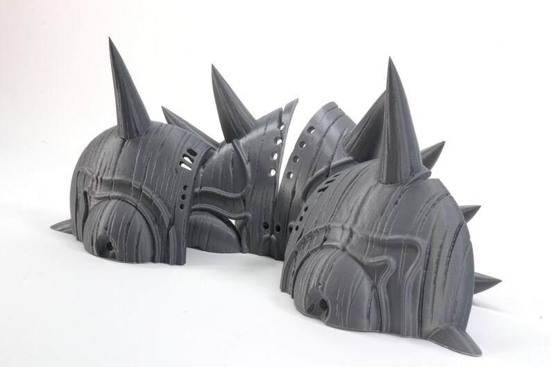 May include: Three gray 3D printed helmets with spikes. The helmets are made of a textured material and have a detailed design.