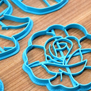 May include: A set of blue plastic cookie cutters in the shapes of a rose, a butterfly, and a circle.