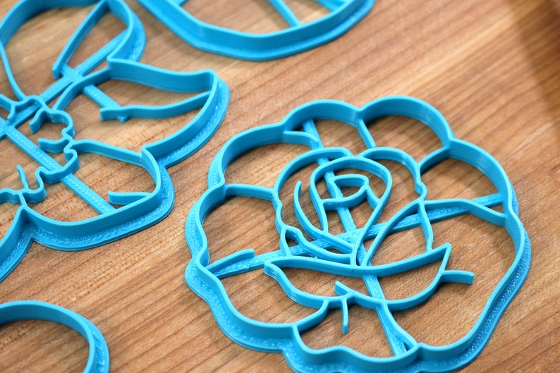 May include: A set of blue plastic cookie cutters in the shapes of a rose, a butterfly, and a circle.