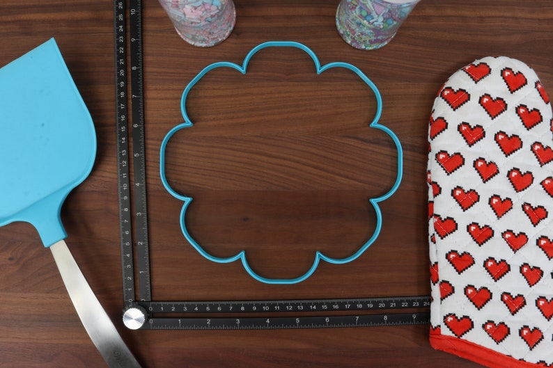 May include: A blue plastic cookie cutter shaped like a flower on a wooden surface. The cookie cutter is 15 cm in diameter.