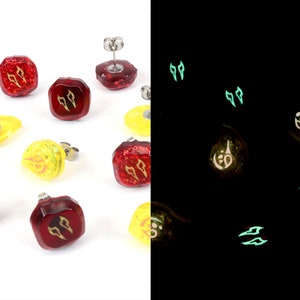May include: A set of eight glow-in-the-dark earrings. Four earrings are red with gold accents and four earrings are yellow with gold accents. The earrings are shaped like a square with rounded corners. The earrings glow green in the dark.