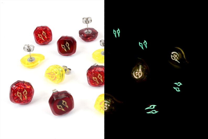 May include: A set of eight glow-in-the-dark earrings. Four earrings are red with gold accents and four earrings are yellow with gold accents. The earrings are shaped like a square with rounded corners. The earrings glow green in the dark.