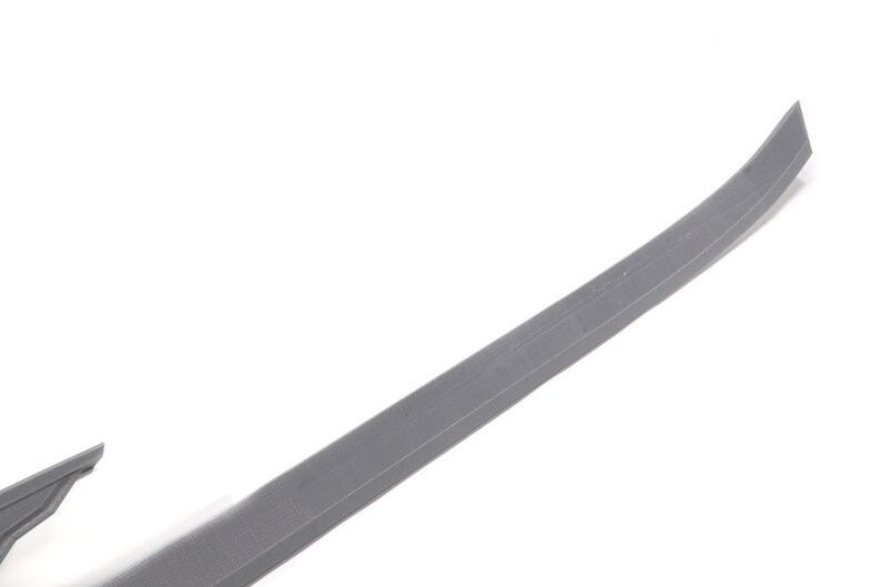 May include: A grey plastic trim piece for a car. The trim piece is curved and has a smooth surface.