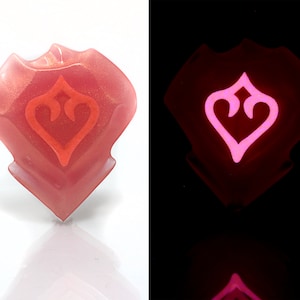 May include: A pink resin heart-shaped charm with a red heart design inside. The charm glows pink in the dark.