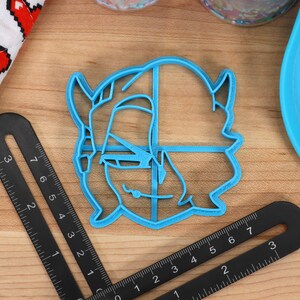 May include: A blue plastic cookie cutter shaped like a cartoon character with horns and a mischievous grin.
