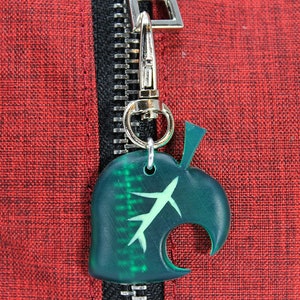 May include: A green leaf-shaped zipper pull with a white stem and a silver metal hook. The zipper pull is attached to a red zipper.