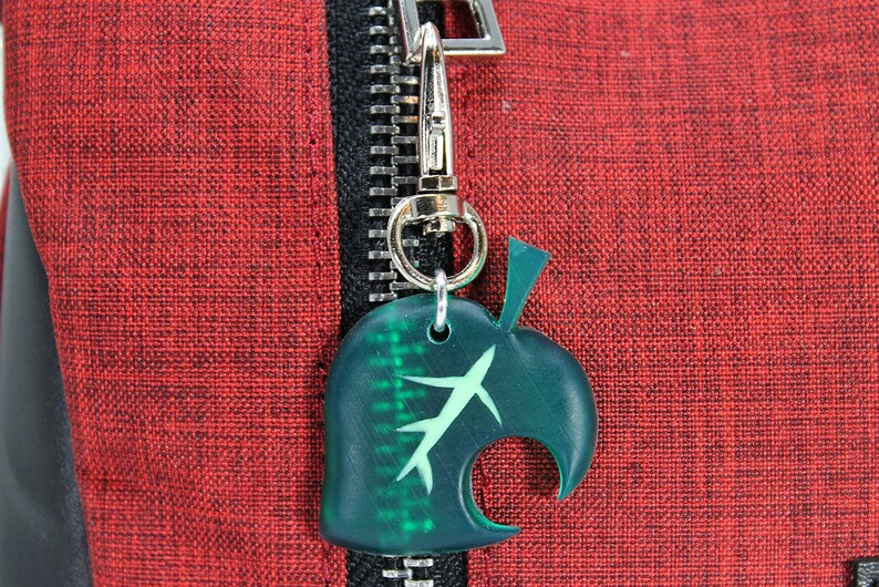 May include: A green leaf-shaped zipper pull with a white stem and a silver metal hook. The zipper pull is attached to a red zipper.