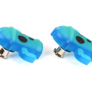 May include: Two blue and green plastic buttons with black dots and a silver pin on the back.
