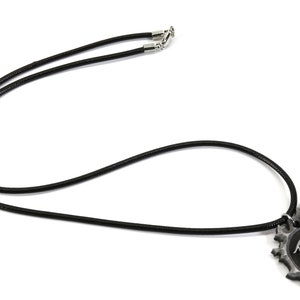 May include: A black leather necklace with a silver pendant featuring a stylized design with a scale and a heart.
