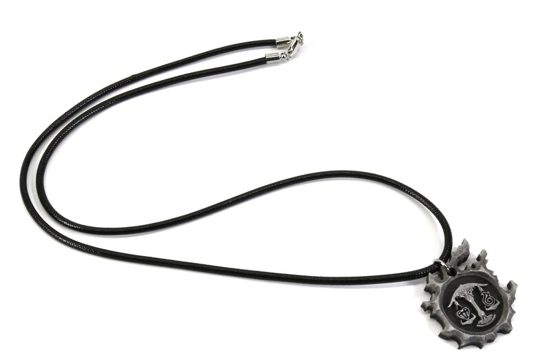 May include: A black leather necklace with a silver pendant featuring a stylized design with a scale and a heart.