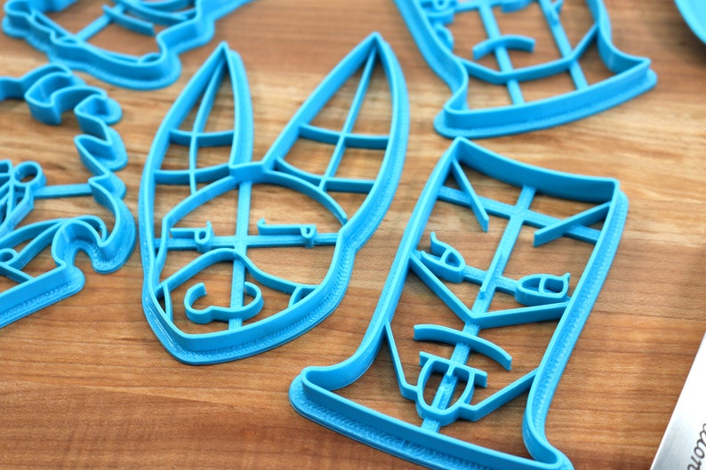 May include: A set of blue plastic cookie cutters shaped like a bunny, a face, and a glass. The cutters are on a wooden surface.