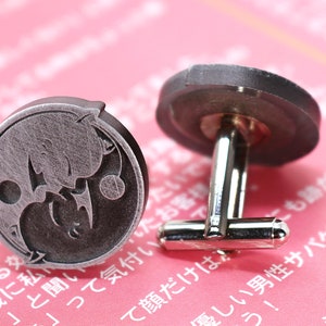 May include: A pair of silver cufflinks with a yin yang design featuring two cats. The cufflinks are on a pink background.