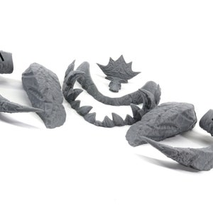 May include: A set of gray plastic model pieces for a monster or creature. The pieces include a head, tail, claws, and teeth.
