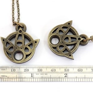 May include: Two gold-toned necklaces with intricate, circular pendants. The pendants feature a geometric design with a central hole. The necklaces are measured against a ruler.