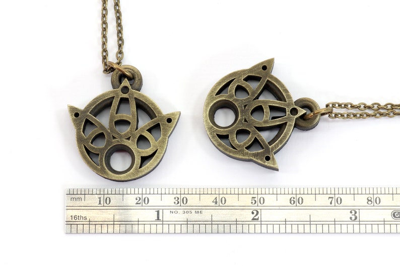 May include: Two gold-toned necklaces with intricate, circular pendants. The pendants feature a geometric design with a central hole. The necklaces are measured against a ruler.