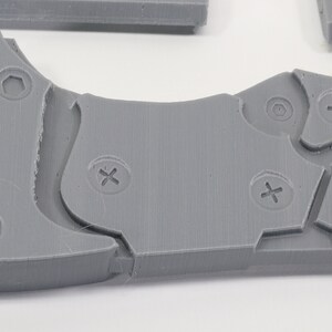 May include: A close-up of a gray plastic object with multiple screw holes and a honeycomb pattern. The object has a textured surface and appears to be part of a larger assembly.