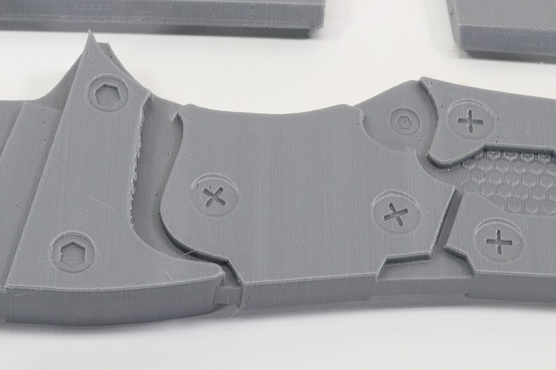 May include: A close-up of a gray plastic object with multiple screw holes and a honeycomb pattern. The object has a textured surface and appears to be part of a larger assembly.
