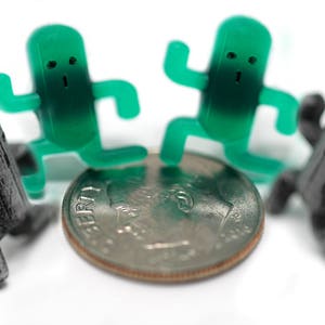 May include: Four small figurines, two green and two black, standing on a silver coin. The green figurines are shaped like people with large heads and small bodies. The black figurines are shaped like people with large heads and small bodies. The coin is a US dime with the words "LIBERTY" and "IN GOD WE TRUST" visible.