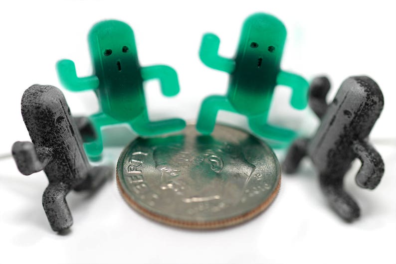 May include: Four small figurines, two green and two black, standing on a silver coin. The green figurines are shaped like people with large heads and small bodies. The black figurines are shaped like people with large heads and small bodies. The coin is a US dime with the words "LIBERTY" and "IN GOD WE TRUST" visible.
