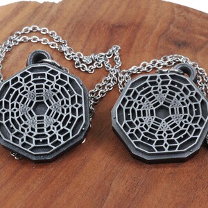 May include: Two silver necklaces with geometric pendant charms. The pendants are octagonal and feature a detailed, intricate design.