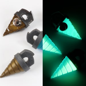 May include: A split image shows three drill-shaped objects. On the left, the objects are gold and gray, with a metallic button. On the right, the objects glow bright teal. The objects have a gray top with a hole.