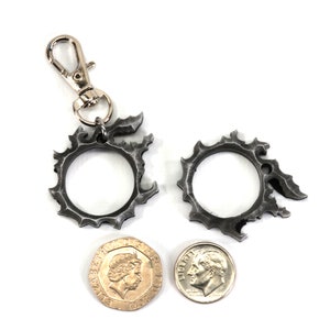 Puede incluir: Dos llaveros de metal plateado en forma de c&iacute;rculo con bordes dentados. Los llaveros son aproximadamente del tama&ntilde;o de una moneda de diez c&eacute;ntimos de euro. Un llavero tiene un cierre de metal plateado.