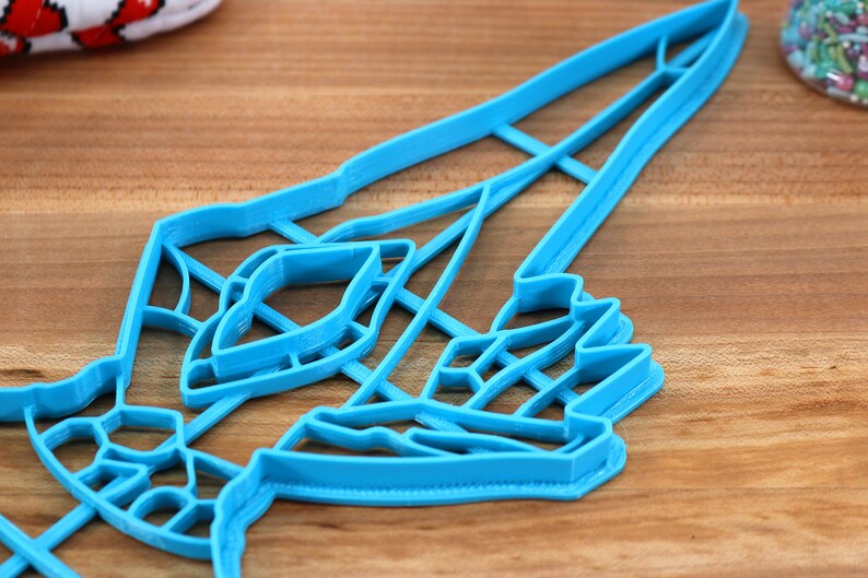 May include: A blue plastic cookie cutter shaped like a rocket ship with a detailed design. The cutter has multiple layers, creating a 3D effect.